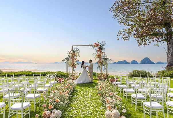 Brautpaar vor einem floralen Traubogen bei seiner Hochzeit im Banyan Tree Krabi mit Blick auf den Strand und das Meer